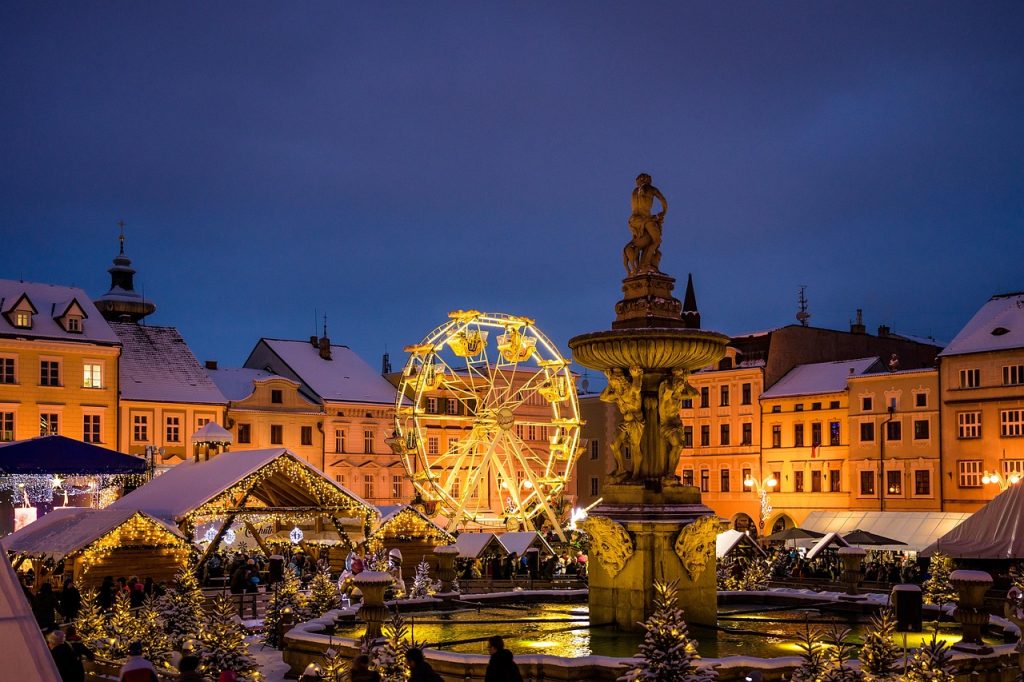Marché de Noël européen illuminé avec grande roue et fontaine au centre d’une place enneigée
