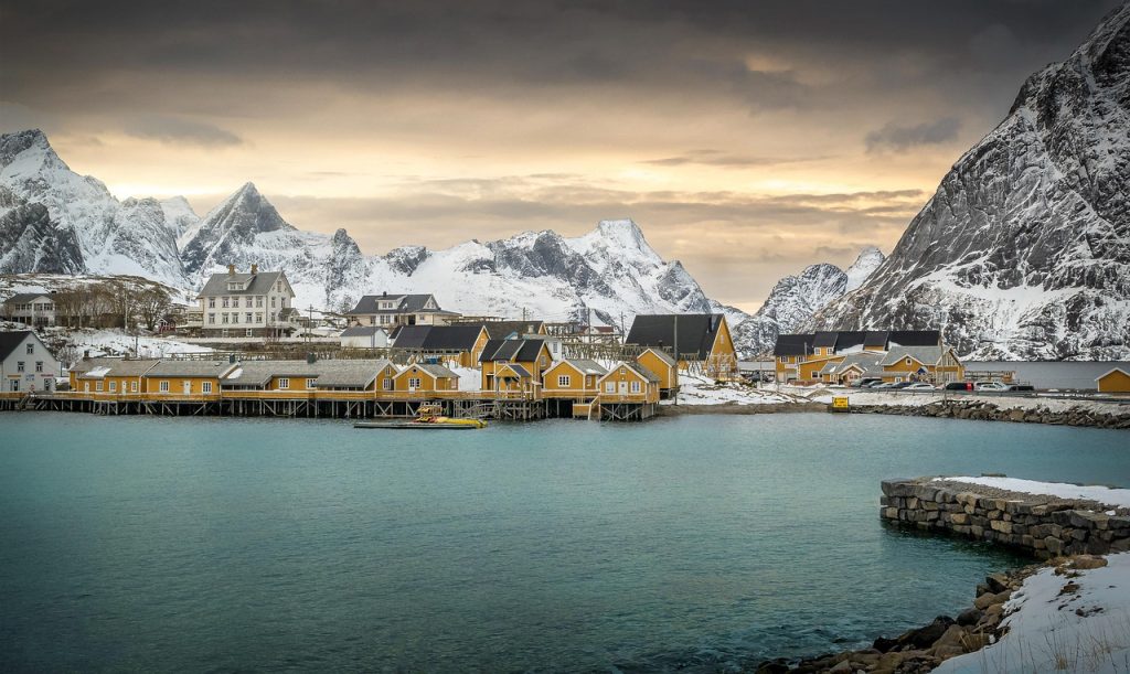 Village norvégien aux maisons jaunes sur pilotis face aux montagnes enneigées des Lofoten.