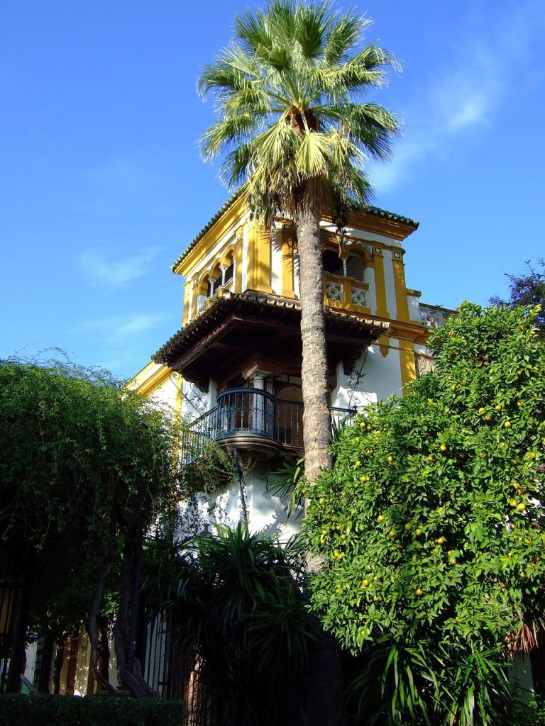 Maison andalouse traditionnelle à Séville avec façade jaune, balcon et palmier sous un ciel bleu.